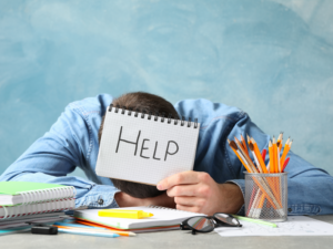 Un homme en burn-out, avachi sur son bureau, tient un papier demandant de l'aide, un soutien psychologique, pour se reconstruire