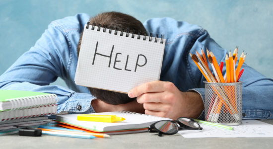 Un homme épuisé, avachi sur son bureau, tient un papier avec le mot "Help" dessus