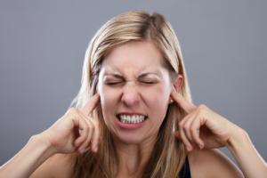 Une femme se bouche les oreilles pour ne pas entendre sa voix critique intérieure. Elle est le signe d'un manque d'estime de soi